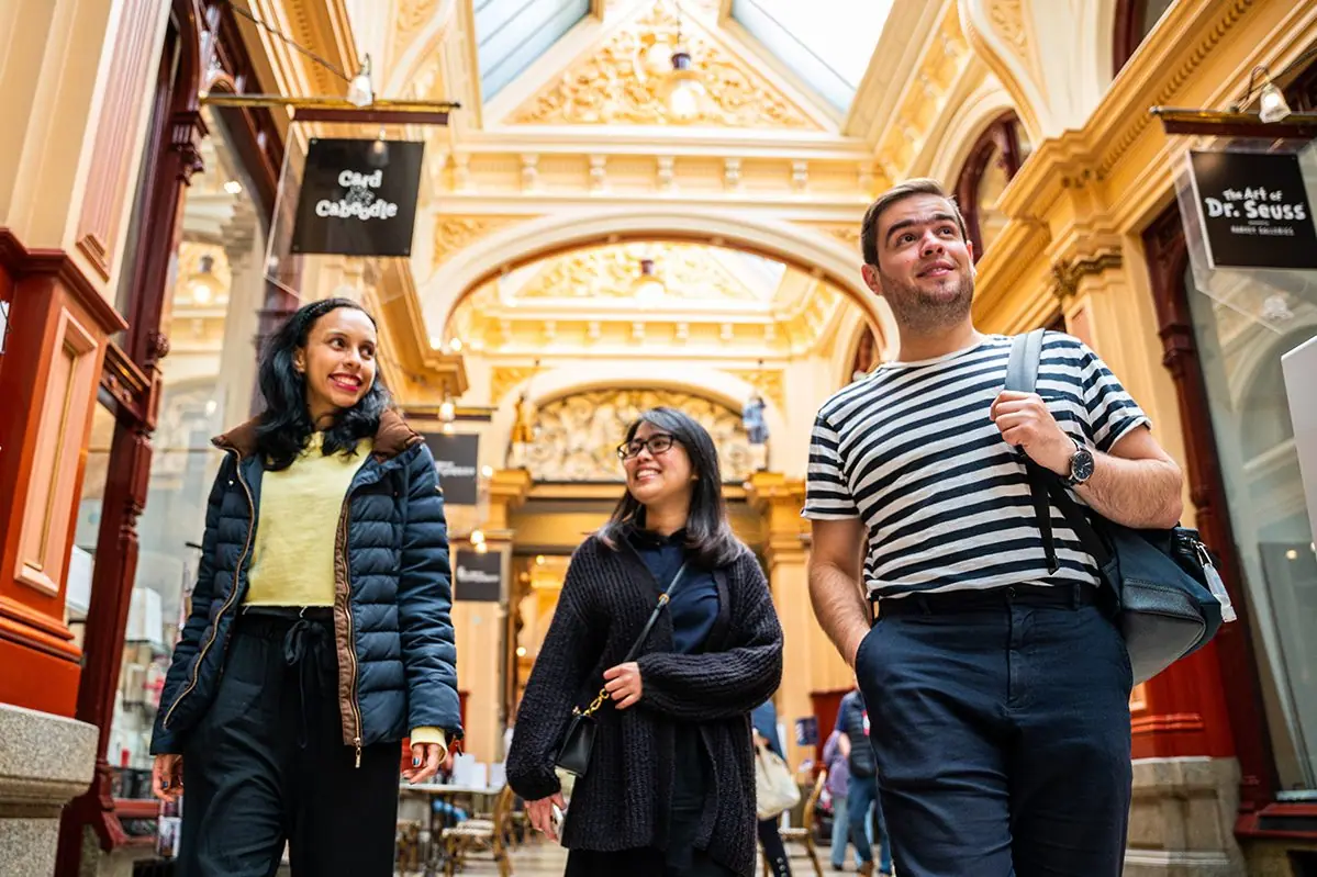 Three friends walking through Melbourne's Block Arcade beneath its ornate gilded ceiling.