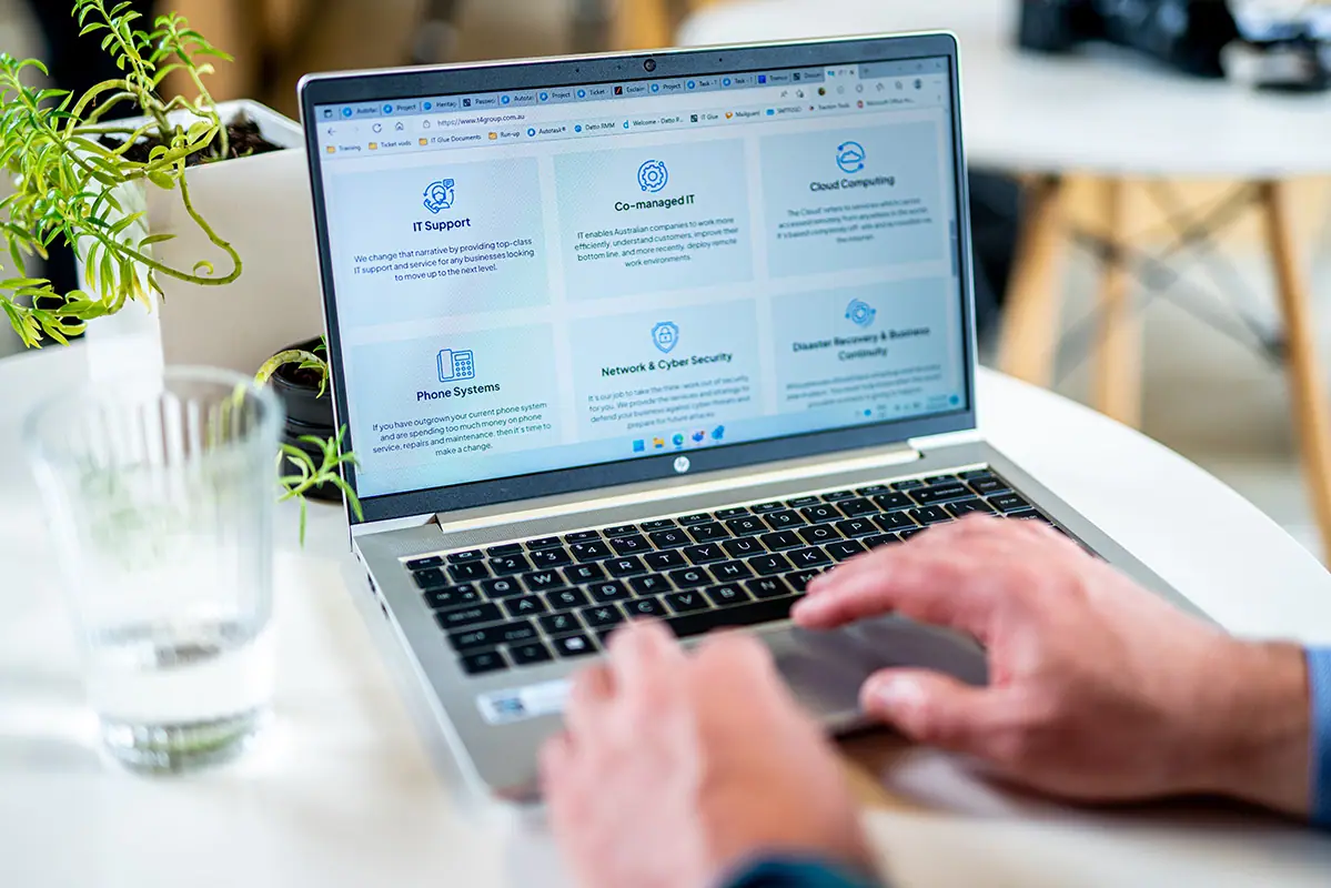 Close-up of hands typing on a laptop showing an IT services website with support and cyber-security panels.