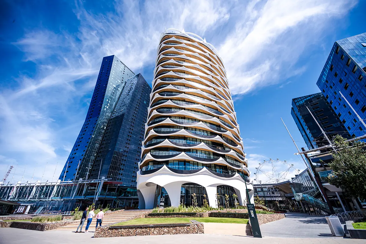 A curved, ribbed apartment tower photographed from below against a blue sky in Melbourne's Docklands.